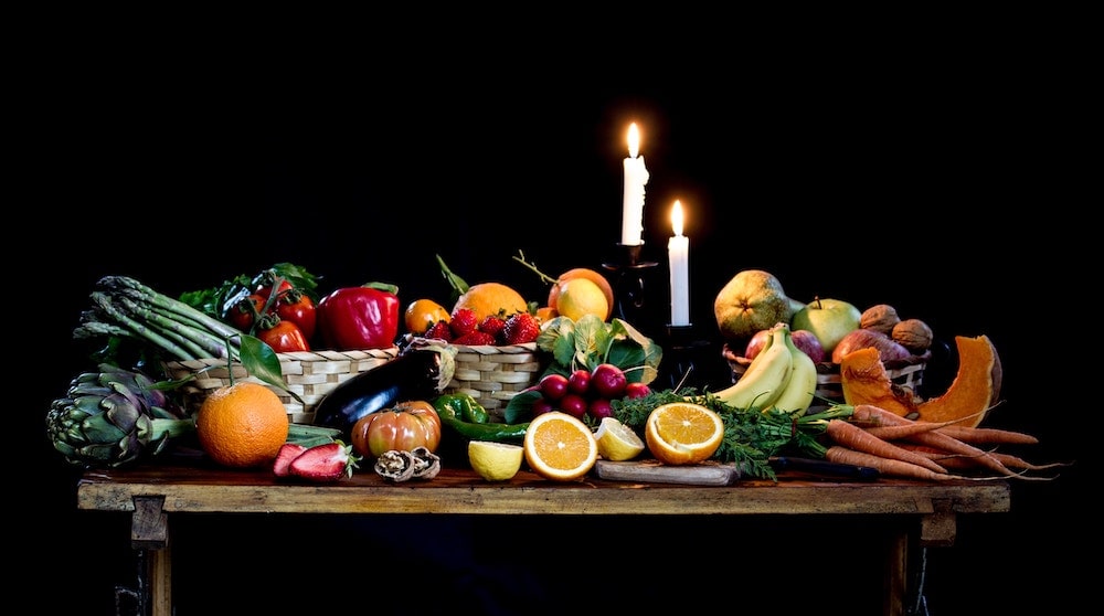 table présentant de nombreux fruits et légumes, éclairée à la bougie